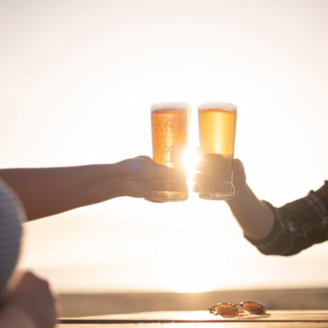 Two people clinking pint glasses of beer together at sunset, sunglasses resting on the table
