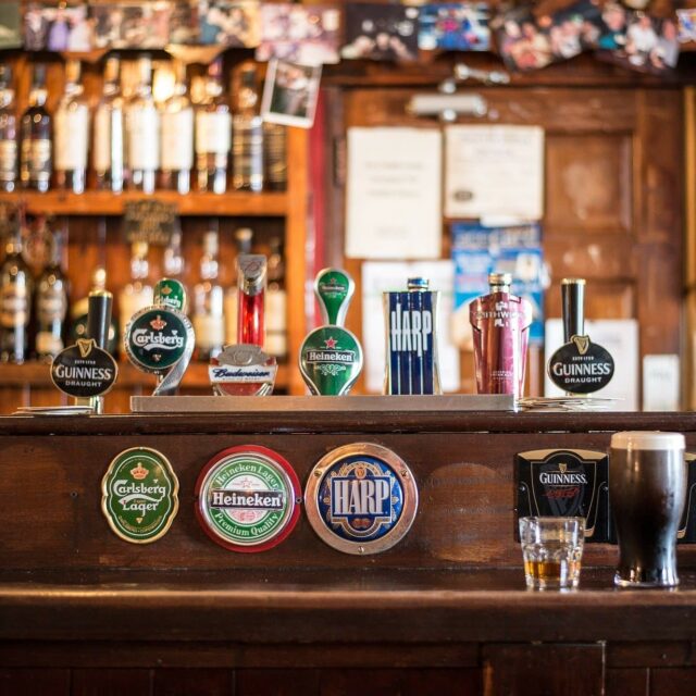 Traditional pub bar with beer taps including Guinness, Carlsberg, Heineken and Harp, shelves of spirits behind