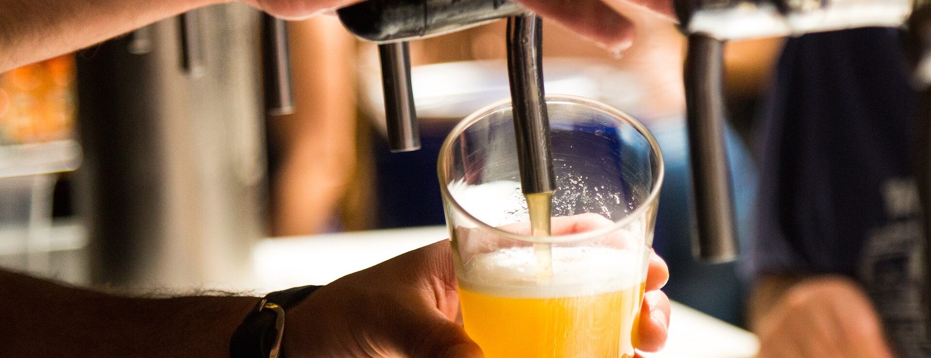 Bartender pouring a draught beer from a tap into a glass at a bar