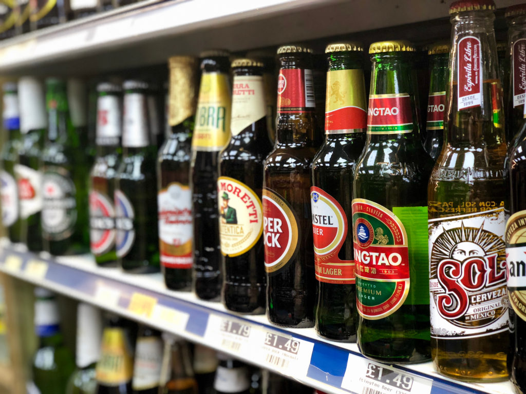 Row of international beer bottles on a shop shelf, including Moretti, Tsingtao and Sol, with price labels below