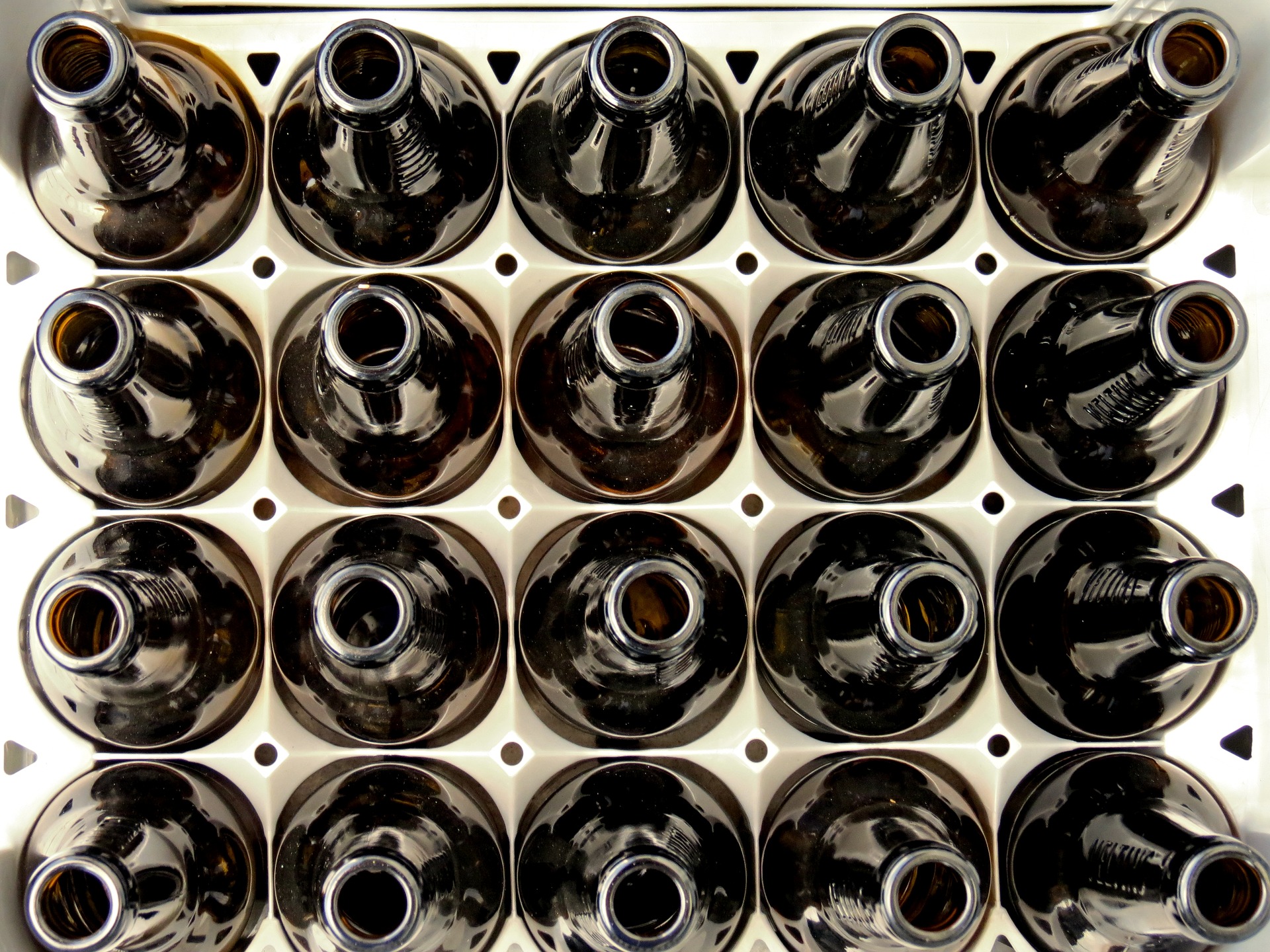 Overhead view of empty brown glass bottles arranged in rows in a white plastic crate