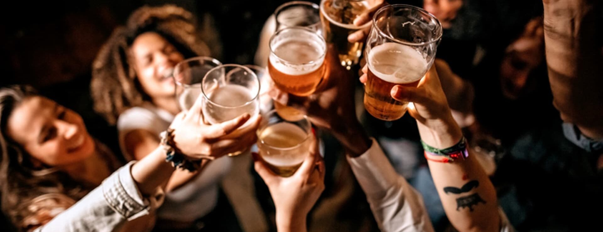 A group of friends raise glasses of beer together in a toast at a dimly lit venue