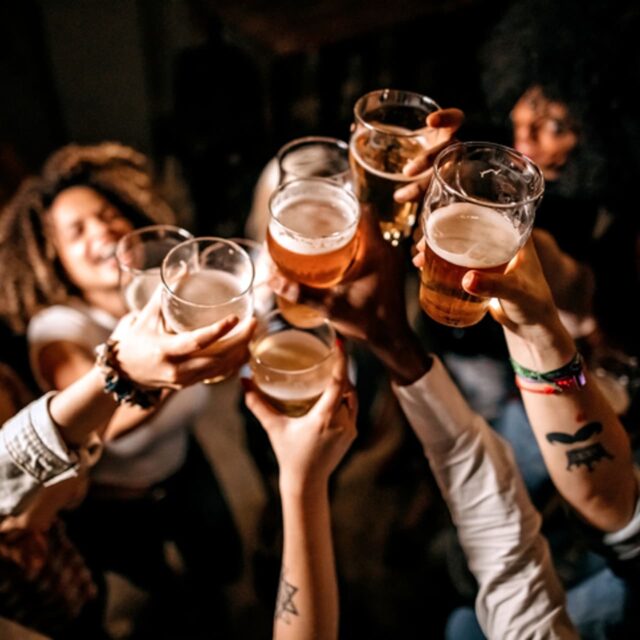 A group of friends raise glasses of beer together in a toast at a dimly lit venue
