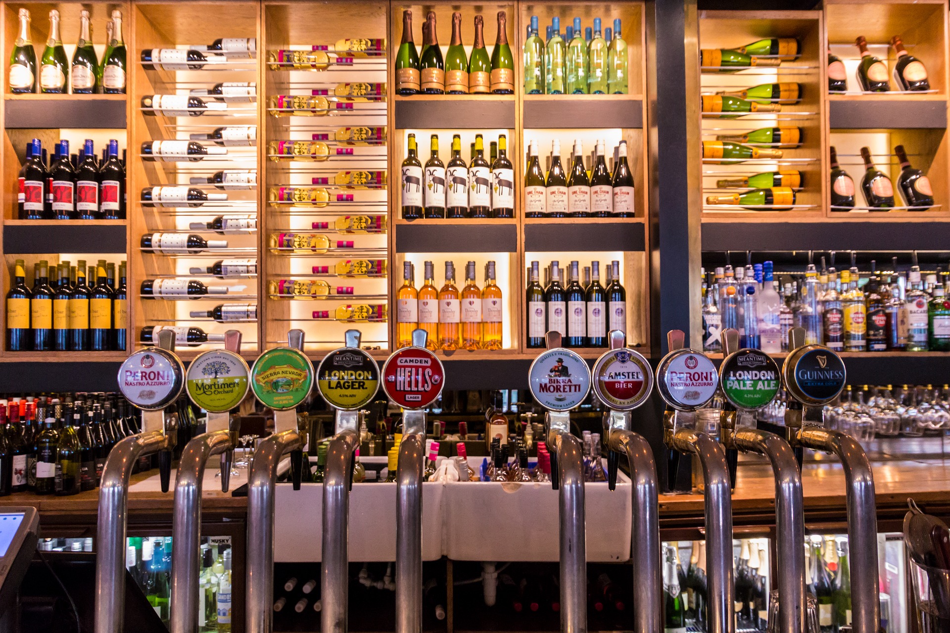 Bar with rows of wine and champagne bottles on shelves above ten beer taps, including Peroni, Guinness, Amstel and London Pale Ale