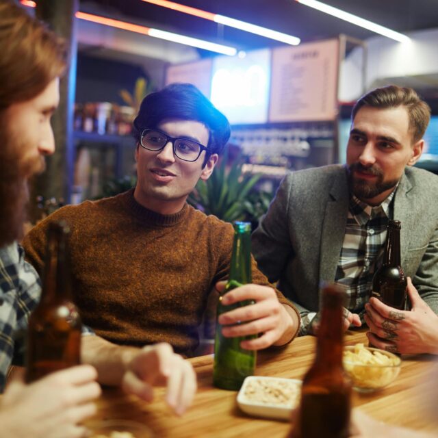 Group of friends chatting and drinking beer together at a bar table with snacks