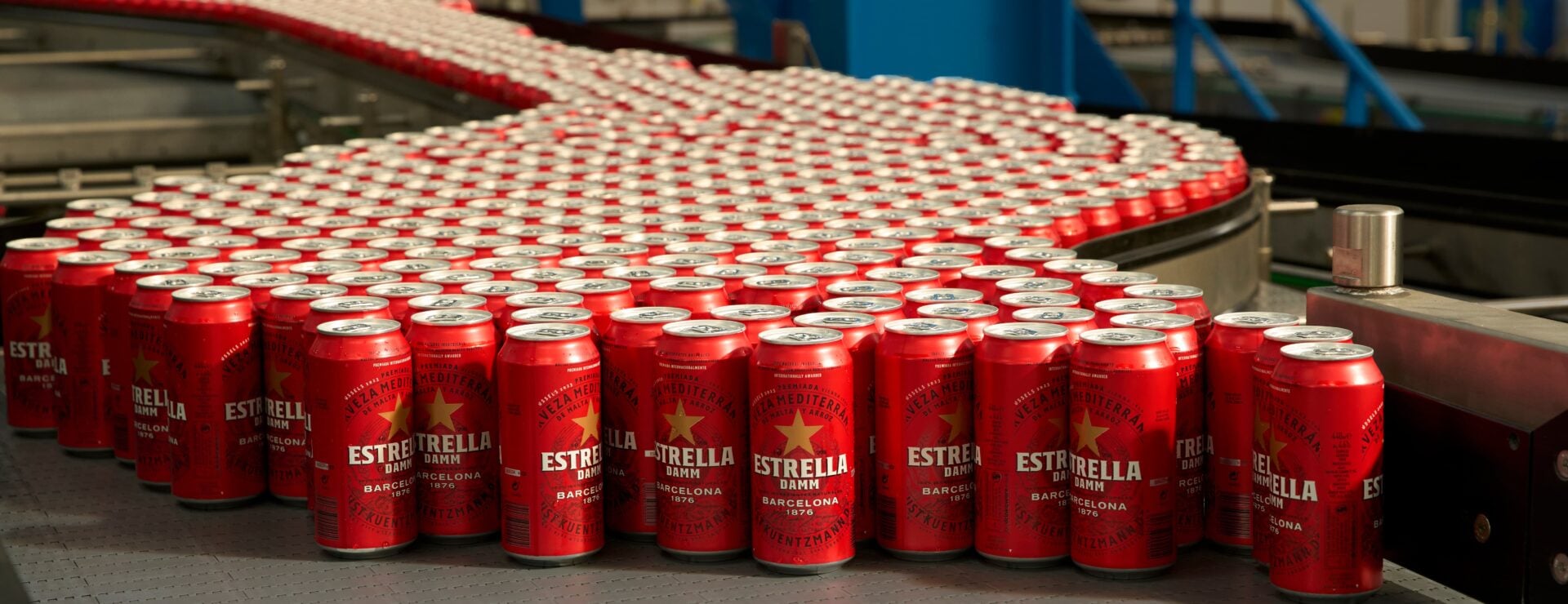 Rows of Estrella Damm beer cans moving along a curved conveyor belt in a bottling factory