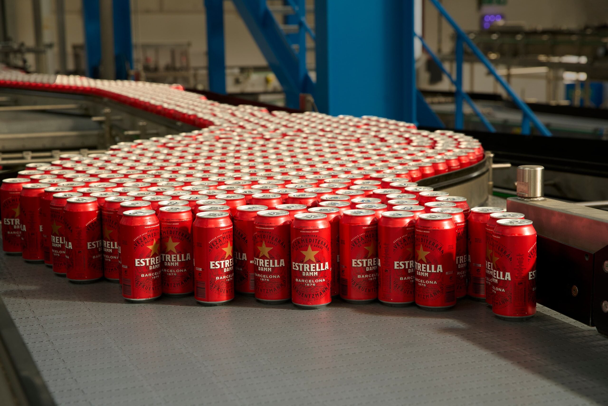 Rows of Estrella Damm beer cans moving along a curved conveyor belt in a bottling factory