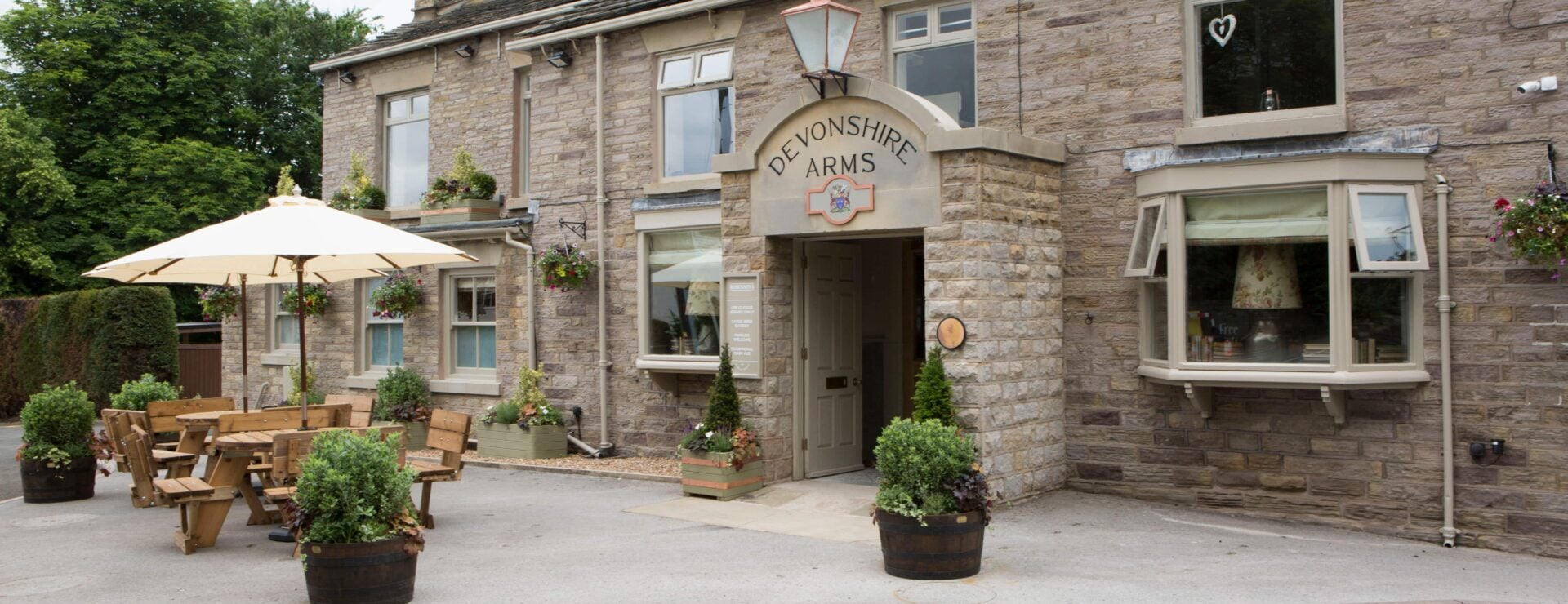 Stone-built Devonshire Arms pub frontage with picnic benches, parasol and potted plants outside