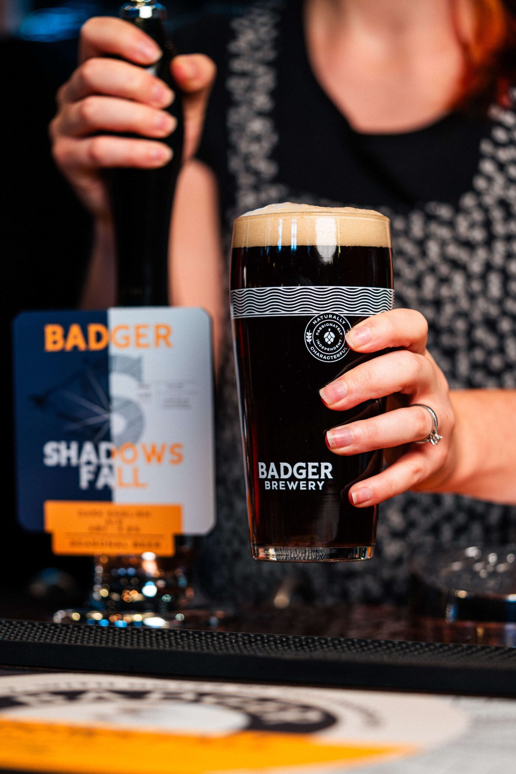 Bar staff pulling a pint of Badger Brewery's Shadows Fall dark ale from the pump