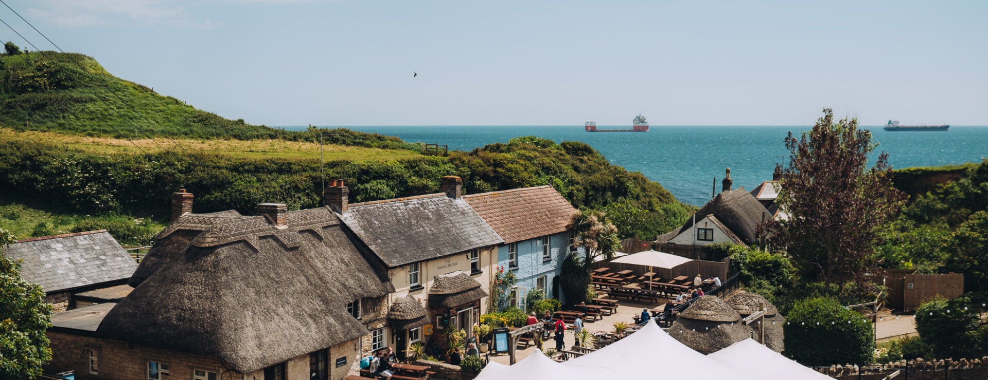 Thatched pub, the Smugglers Inn, in a coastal cove with sea view and tankers offshore