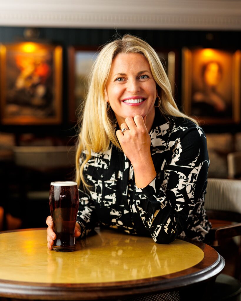 Woman smiling at a pub table, holding a pint of beer