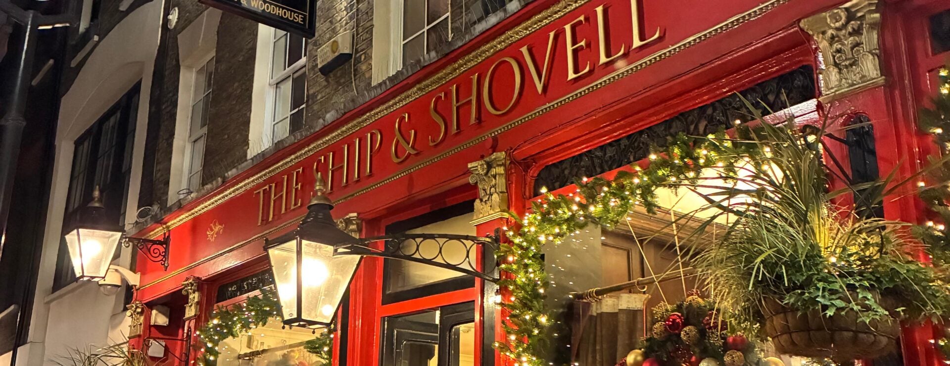 People gathered outside The Ship & Shovell pub in London, its red frontage decorated with Christmas garlands and lights at night