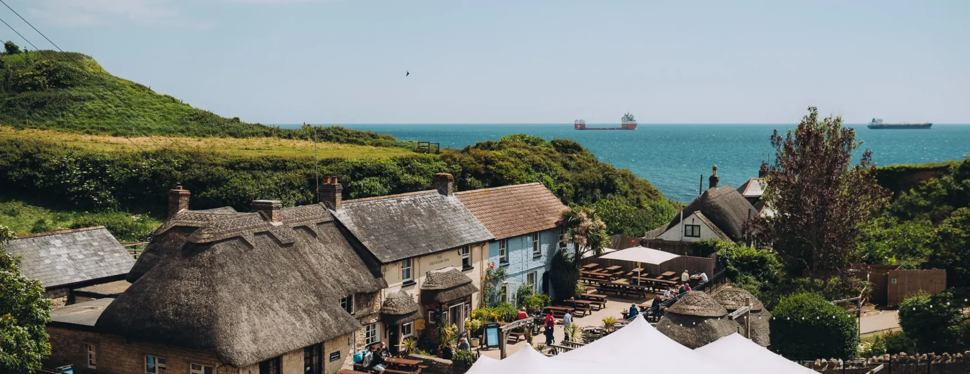 Thatched pub, the Smugglers Inn, in a coastal cove with sea view and tankers offshore
