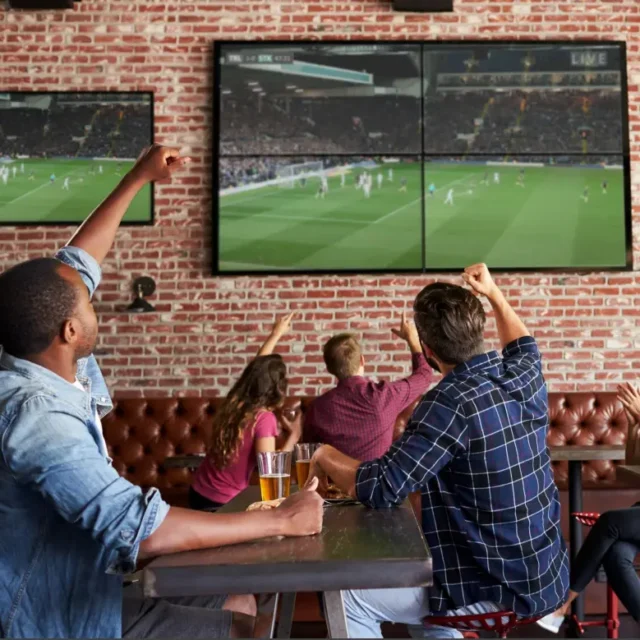 Friends cheering with raised arms while watching a live football match on screens in a pub